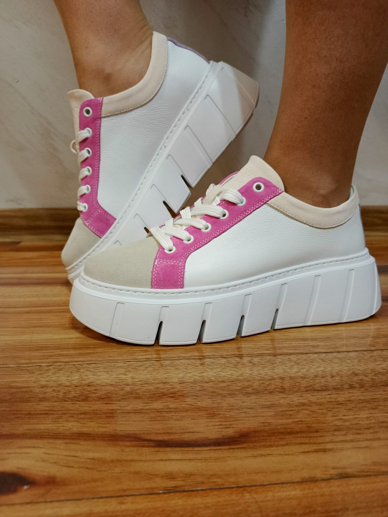 White platform sneakers with pink accents and chunky soles on wooden floor