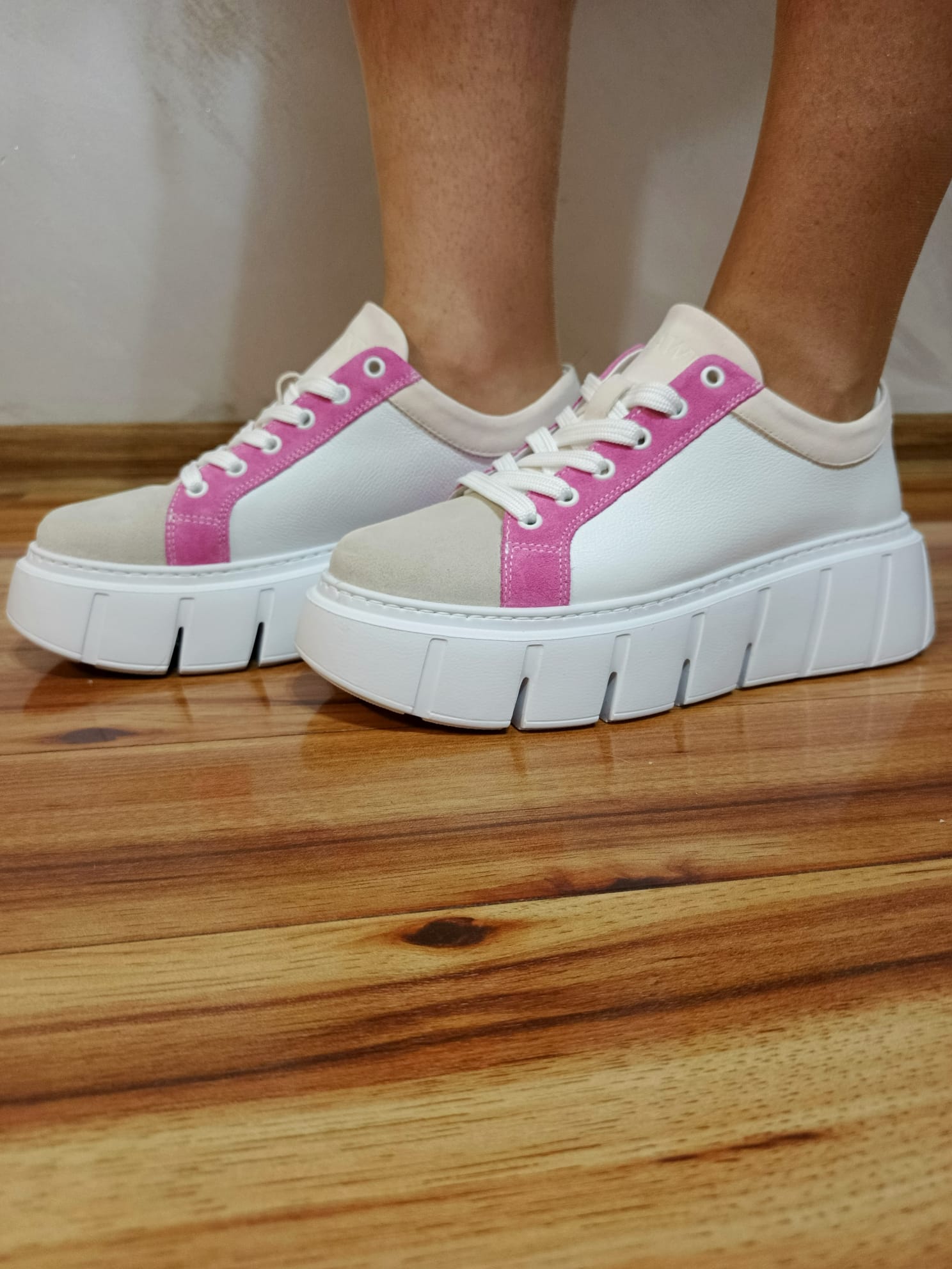 Handmade leather sneakers with thick white soles, pink accents, beige toe, on wooden floor