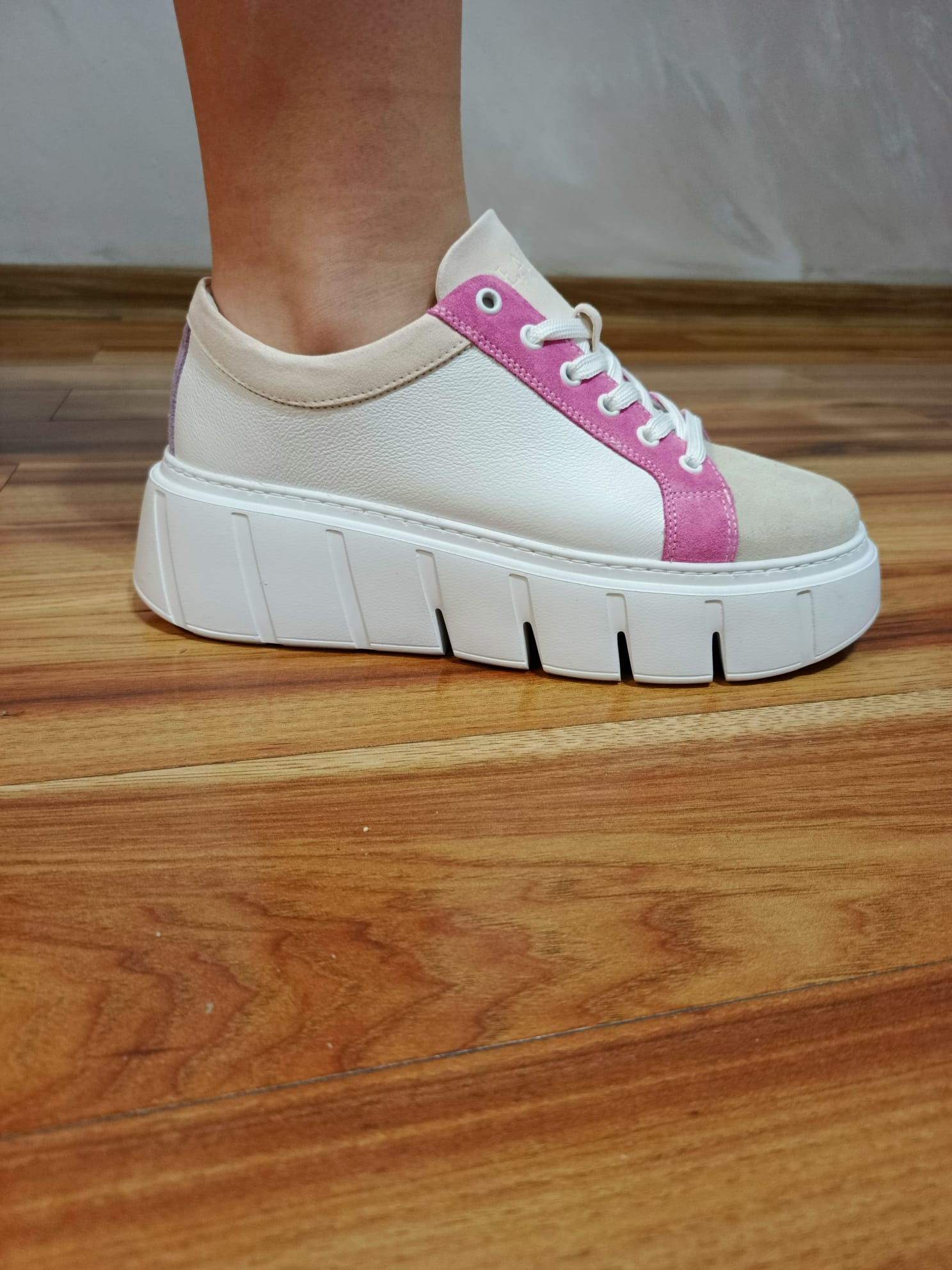 White leather platform sneaker with pink suede accents on wooden floor