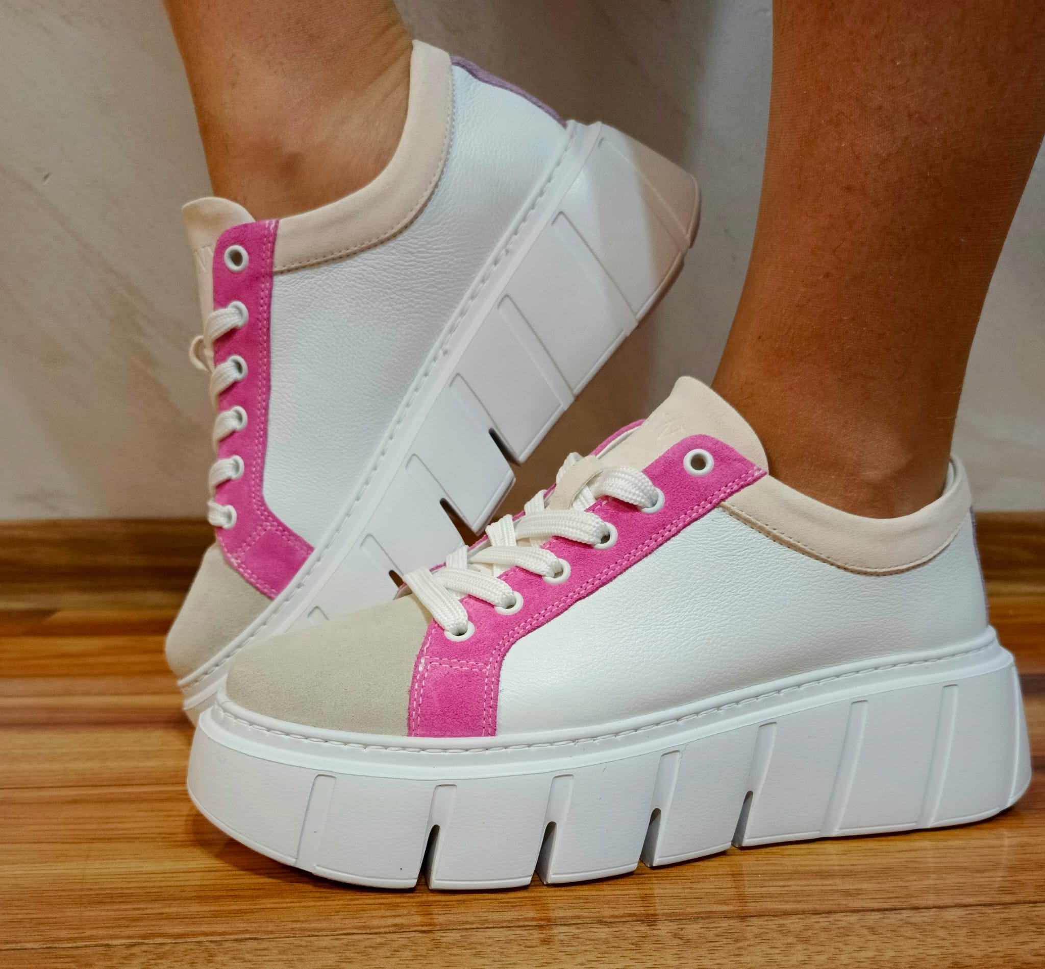 White leather platform sneakers with pink suede accents and chunky soles on wooden floor